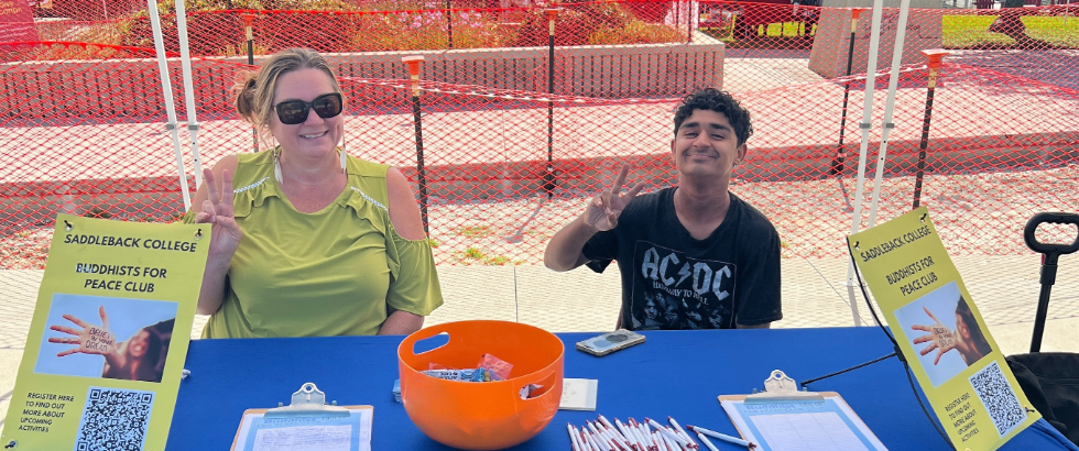 two adults sitting at a table outside with candy and club information
